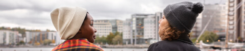 Two girls looking at each other with a river and buildings in the background