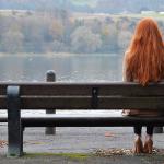 Long red haired woman sitting bench lake