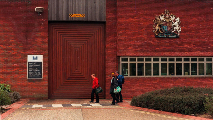 A photograph showing the exterior of Feltham Young Offender Institution with three people in the foreground